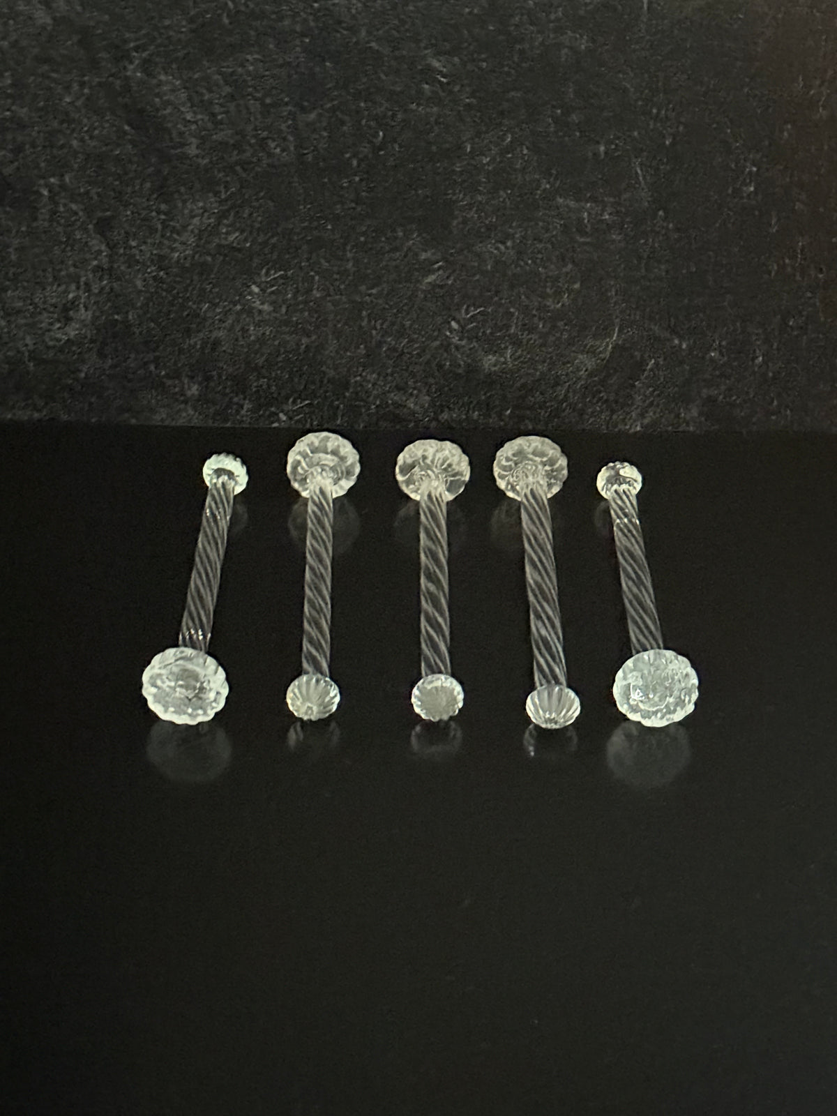 Close-up of a set of spiral glass cocktail muddlers on a black background