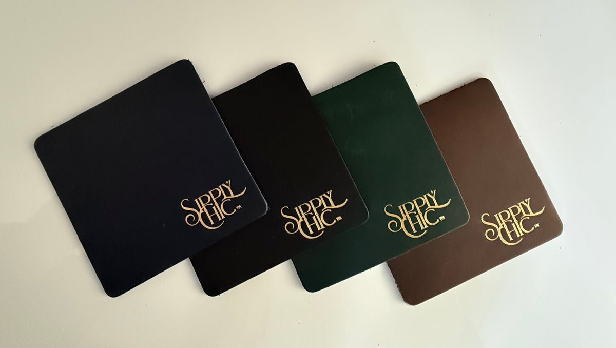 Four square leather coasters in brown, dark green, black, and navy, arranged diagonally on a light beige surface. Each piece features the word 'Sipply Chic' in a gold cursive script.
