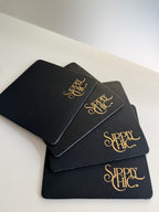 Four navy square coasters stacked on a white surface, each printed with the phrase 'Sipply Chic' in a metallic gold script.