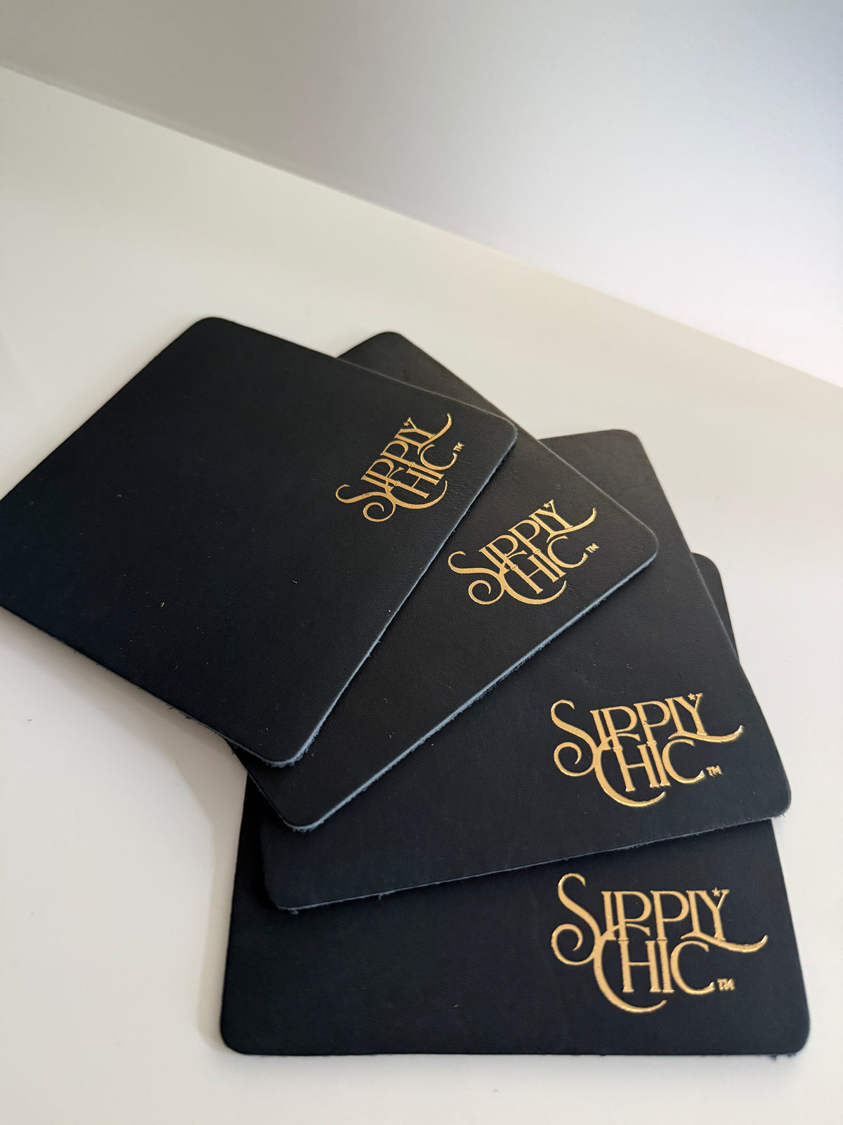 Four navy square coasters stacked on a white surface, each printed with the phrase 'Sipply Chic' in a metallic gold script.
