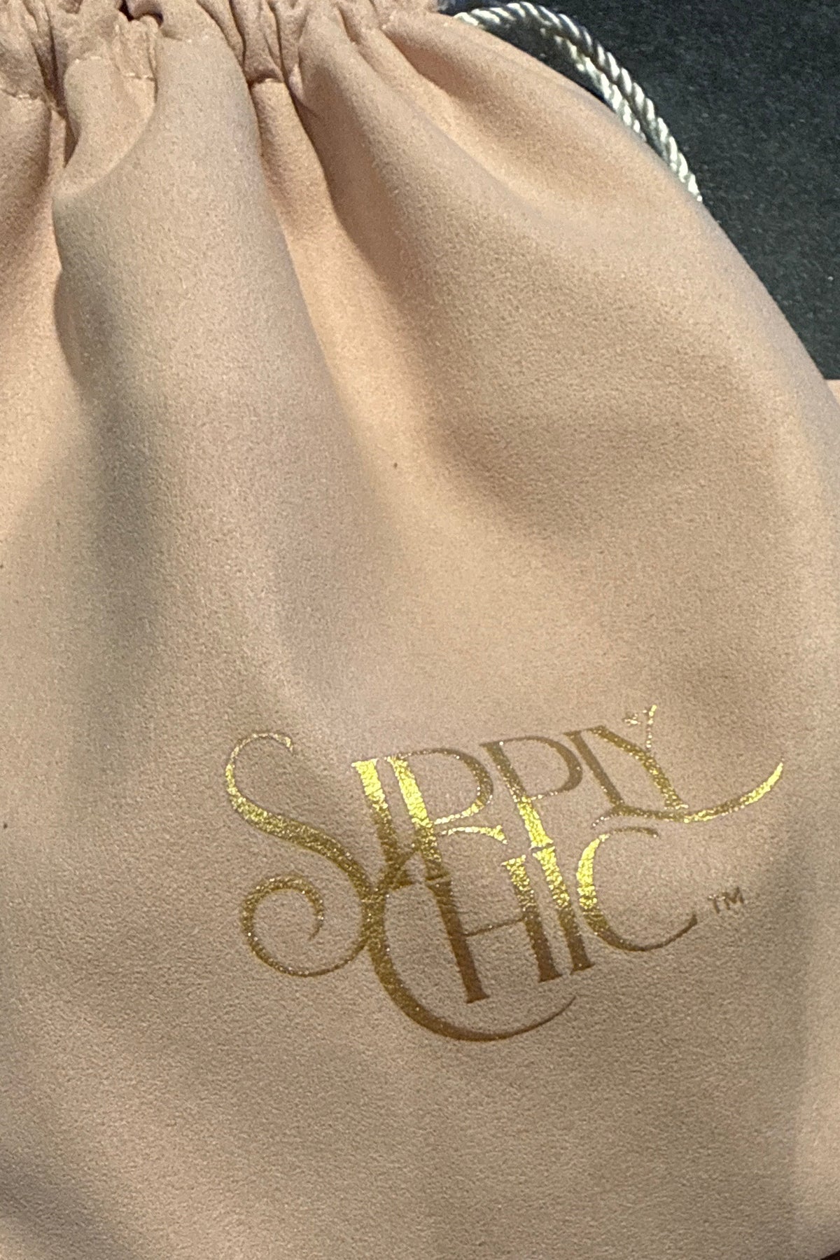 A beige drawstring dust bag with metallic gold foil 'Sipply Chic' branding,