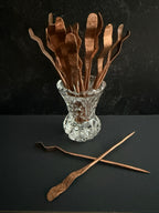 Set of copper cocktail picks in a clear glass holder on a dark surface.