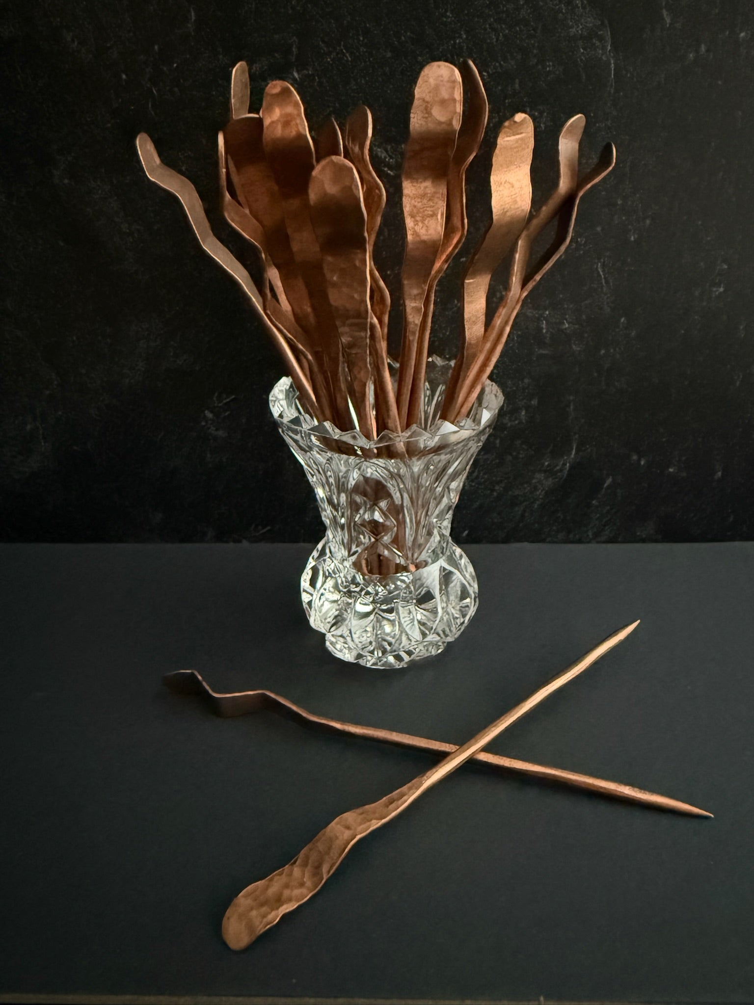 Set of copper cocktail picks in a clear glass holder on a dark surface.
