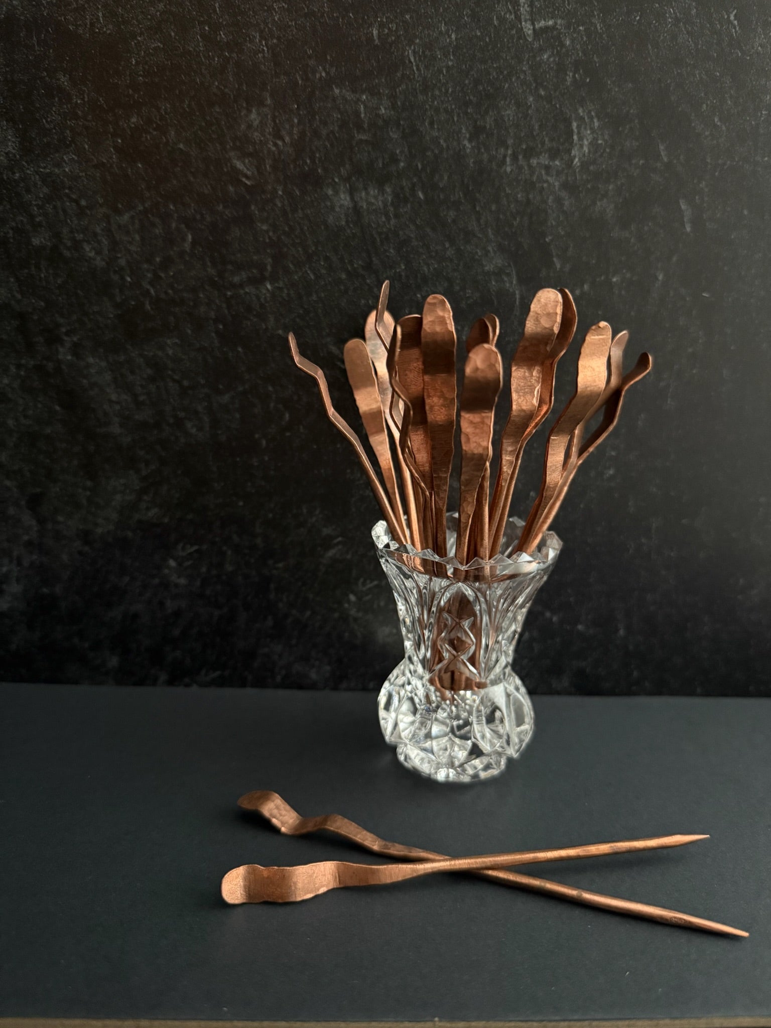 Copper bar tools in a glass container on a dark surface
