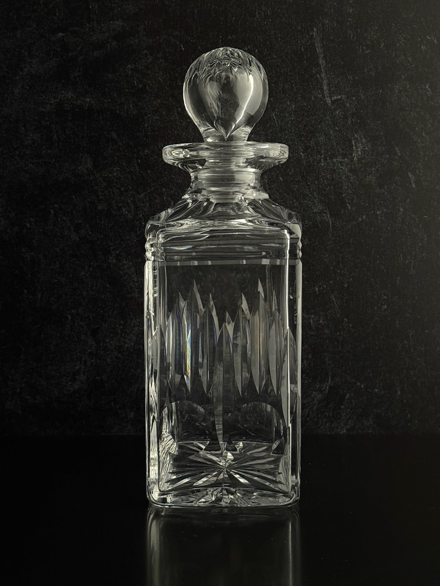 Clear glass decanter with a spherical stopper on a black background