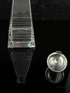 A closeup photo of crystal decanter base with horizontal ridges, shown alongside a matching round clear stopper on a glossy black reflective surface.