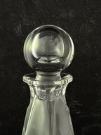 A clear glass decanter with a spherical glass stopper, shown against a dark textured background.
