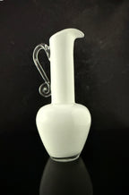 A white frosted glass pitcher with a curved handle, set against a dark reflective background.