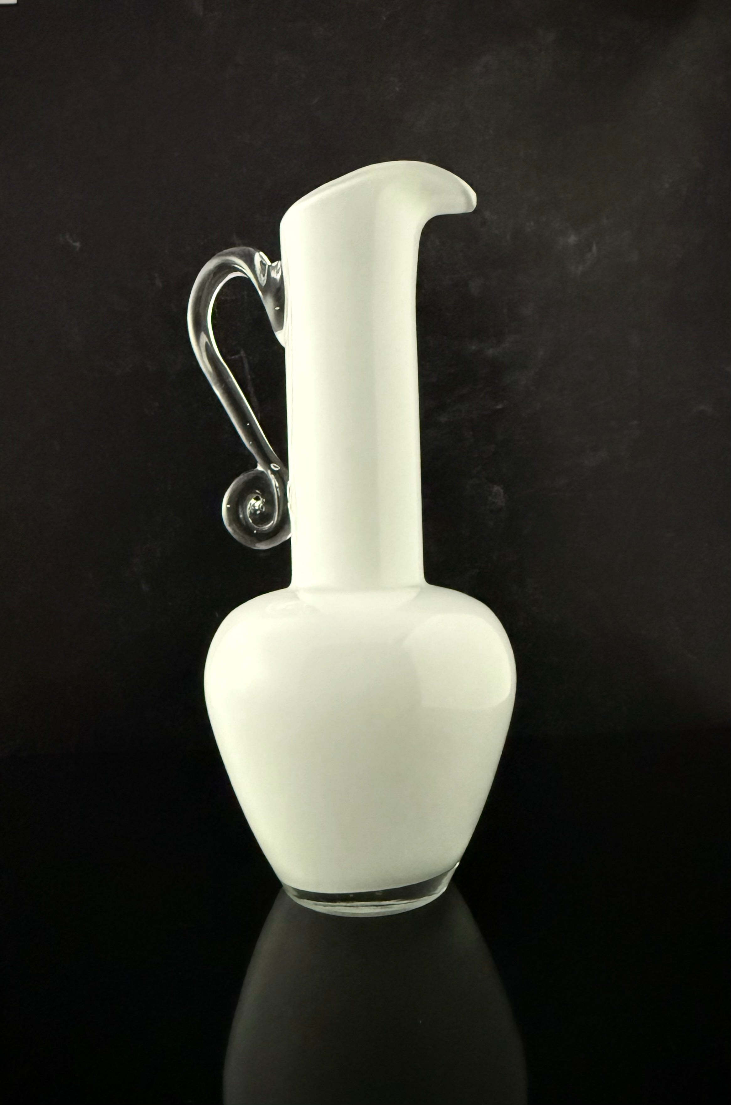 A white frosted glass pitcher with a curved handle, set against a dark reflective background.