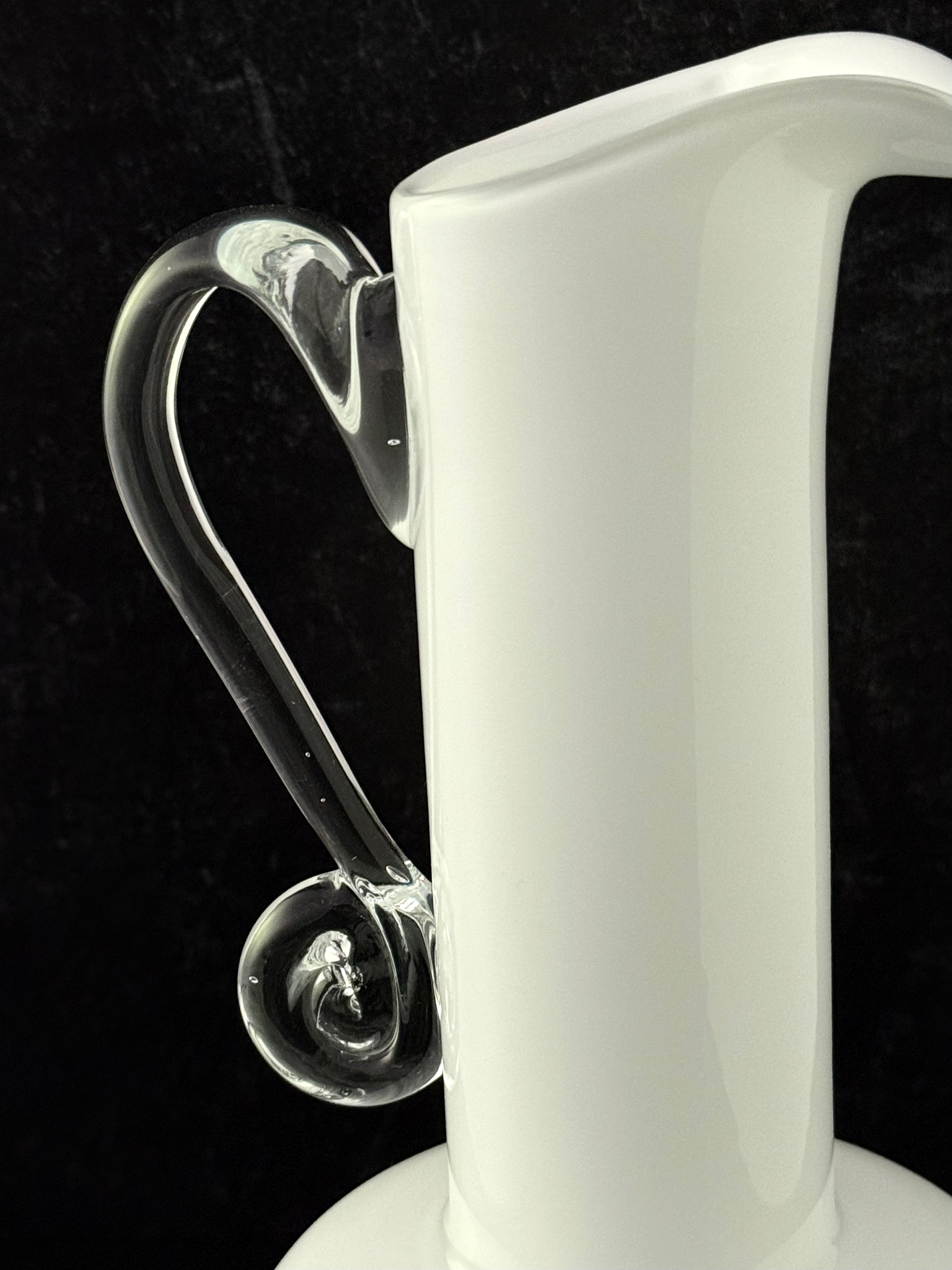 A close-up of a white glass vessel with a clear curved handle and a small bubble detail, set against a black background.