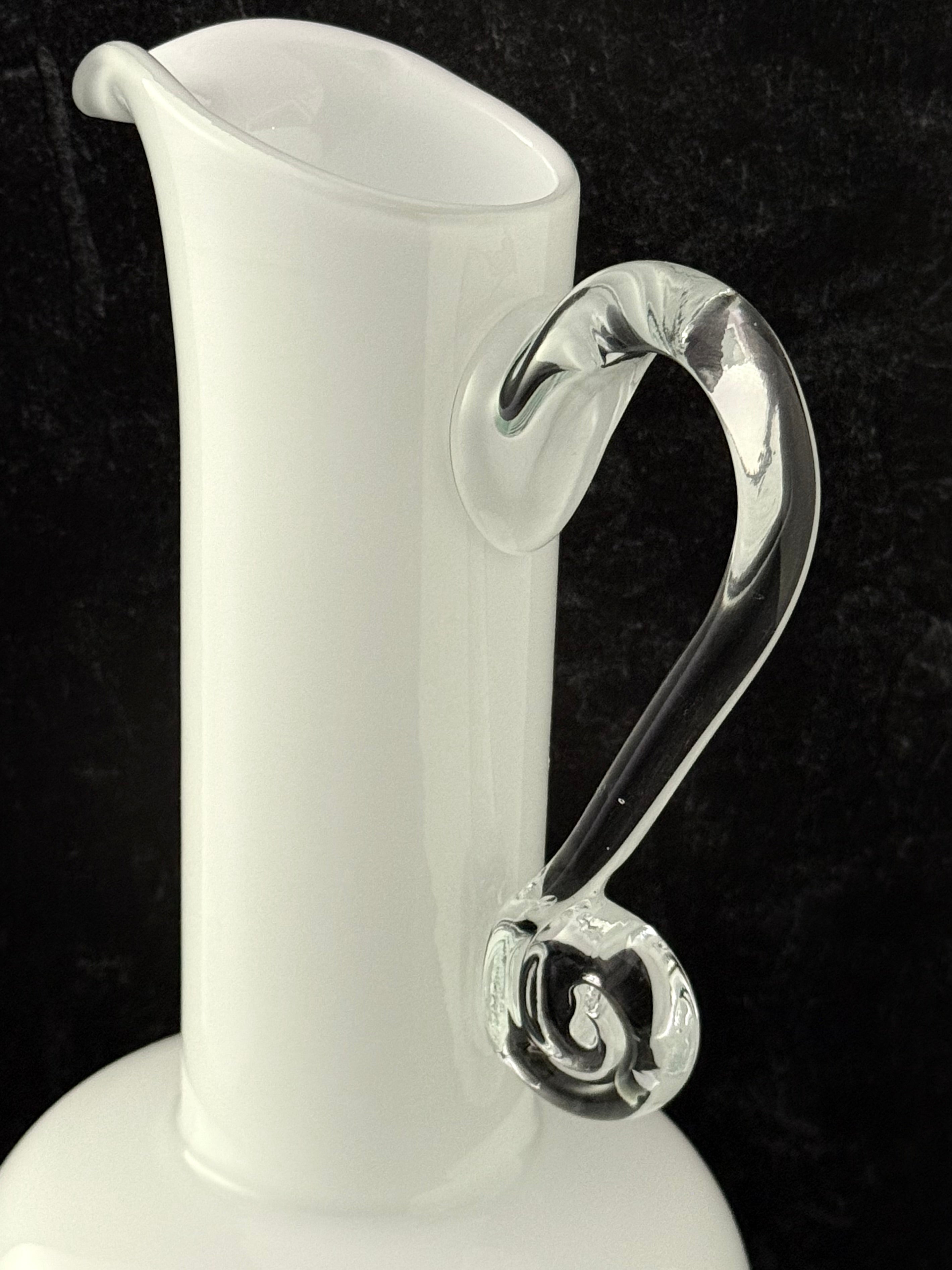 A white glass pitcher with a curved, clear glass handle, shown against a dark black background.
