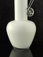 A white glass bottle or vase with a bulbous rounded body, a narrow neck, and a clear glass curved attachment near the top, photographed against a black background.