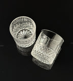 Two clear cut-crystal tumbler glasses with faceted geometric patterns, displayed on a reflective black surface.