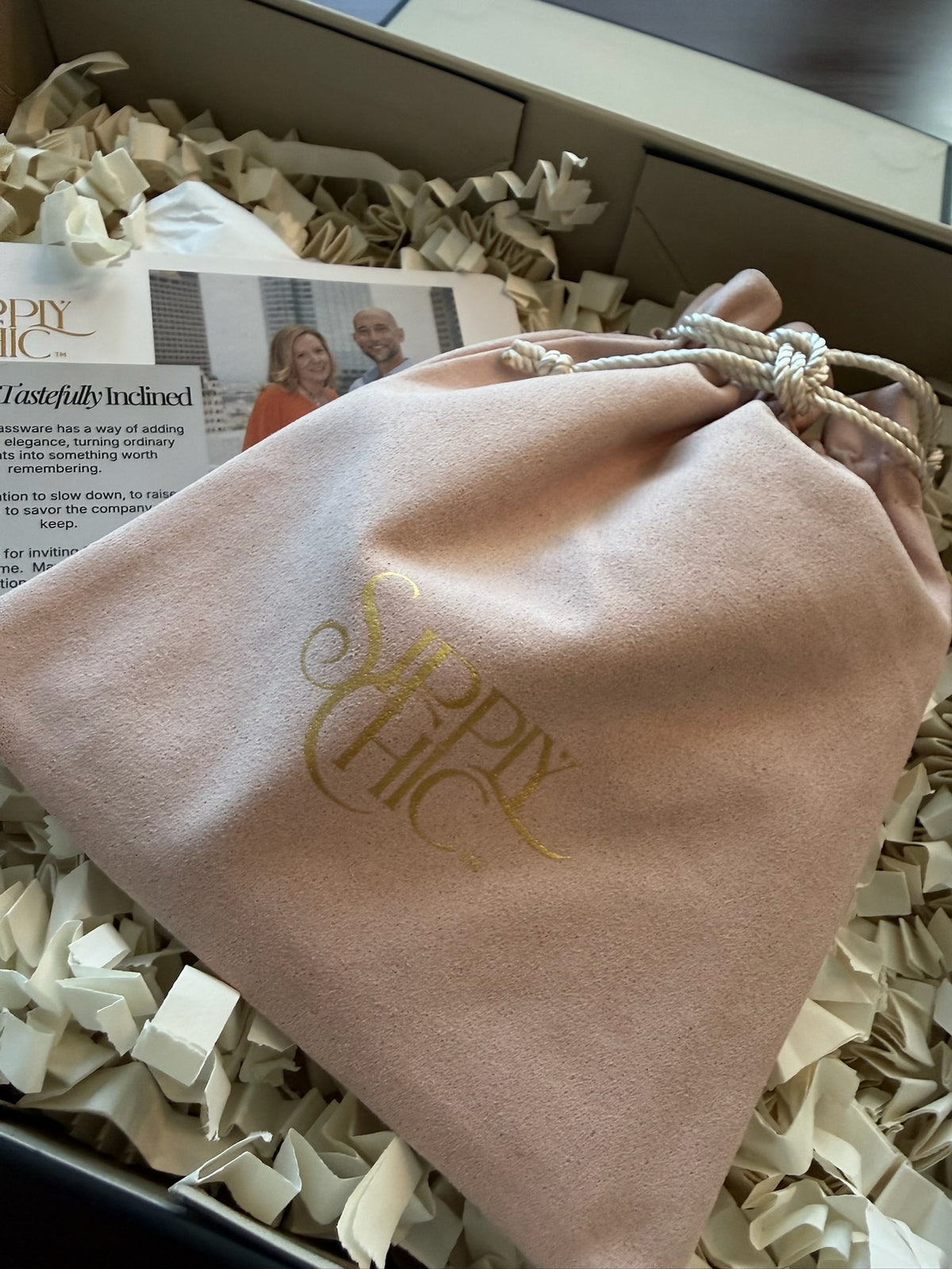 A blush pink velvet drawstring pouch with gold foil 'Sipply Chic' branding, nestled in crinkle paper inside a gift box.