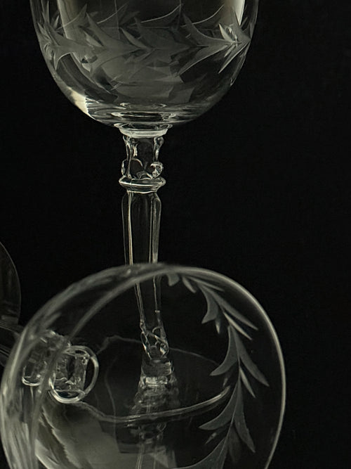 Close-up studio shot of a clear etched glass wine glass against a black background, showing the bowl and stem with decorative leaf-like engraving.