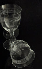 Two clear etched glass goblets with decorative bands, shown on a black reflective surface.