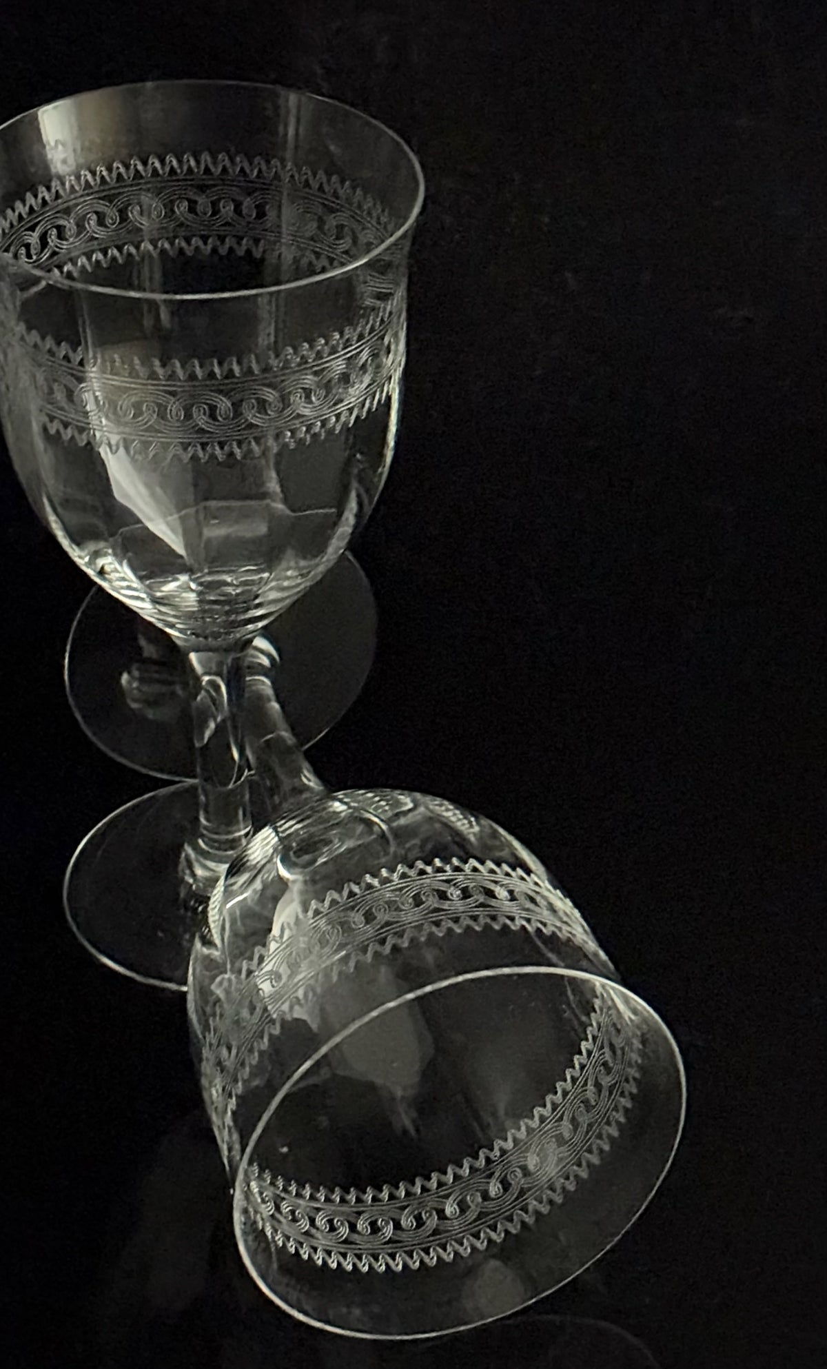 Two clear etched glass goblets with decorative bands, shown on a black reflective surface.
