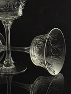 Clear cut crystal wine glasses with ornate floral engravings, photographed on a glossy black reflective surface against a black background.