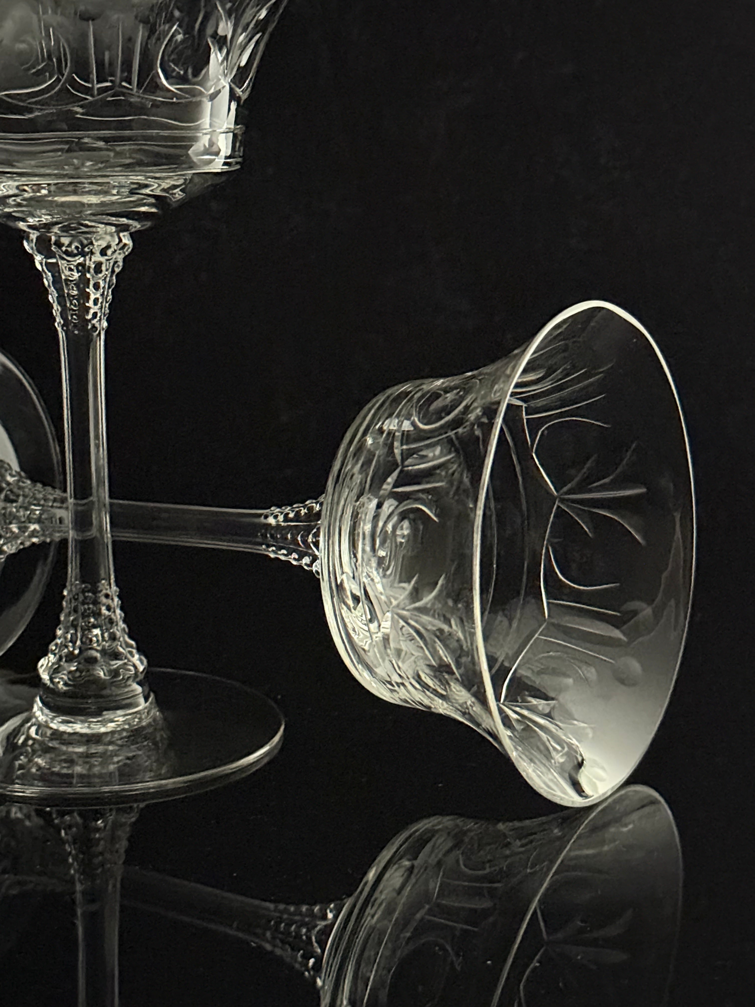 Clear cut crystal wine glasses with ornate floral engravings, photographed on a glossy black reflective surface against a black background.