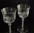 Two clear cut-crystal wine glasses with etched floral and geometric patterns, standing against a solid black background.