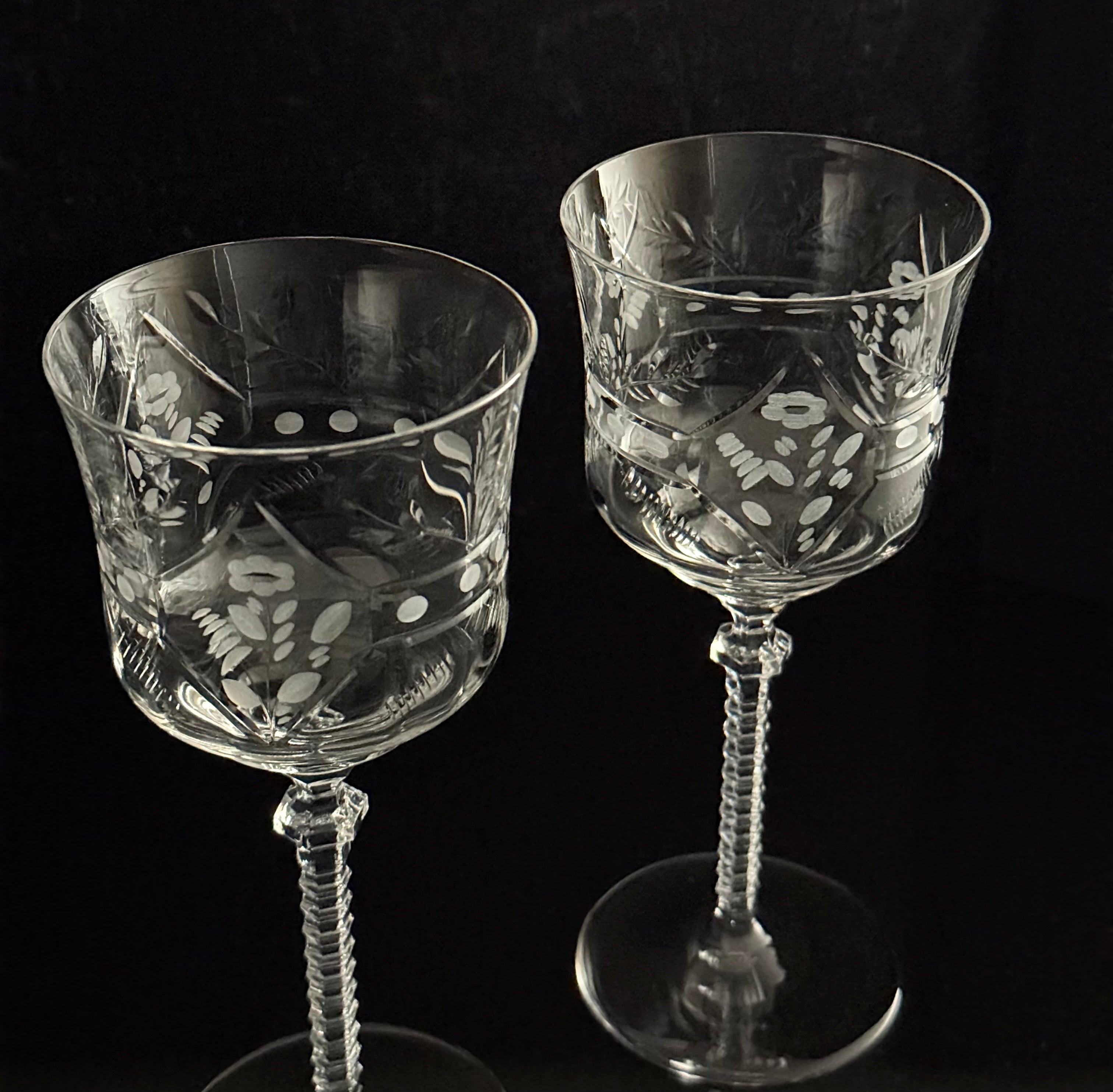 Two clear cut-crystal wine glasses with etched floral and geometric patterns, standing against a solid black background.