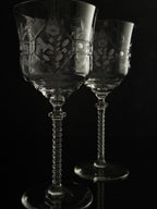Two clear cut-glass wine glasses with floral engravings and twisted stems, photographed against a black background.