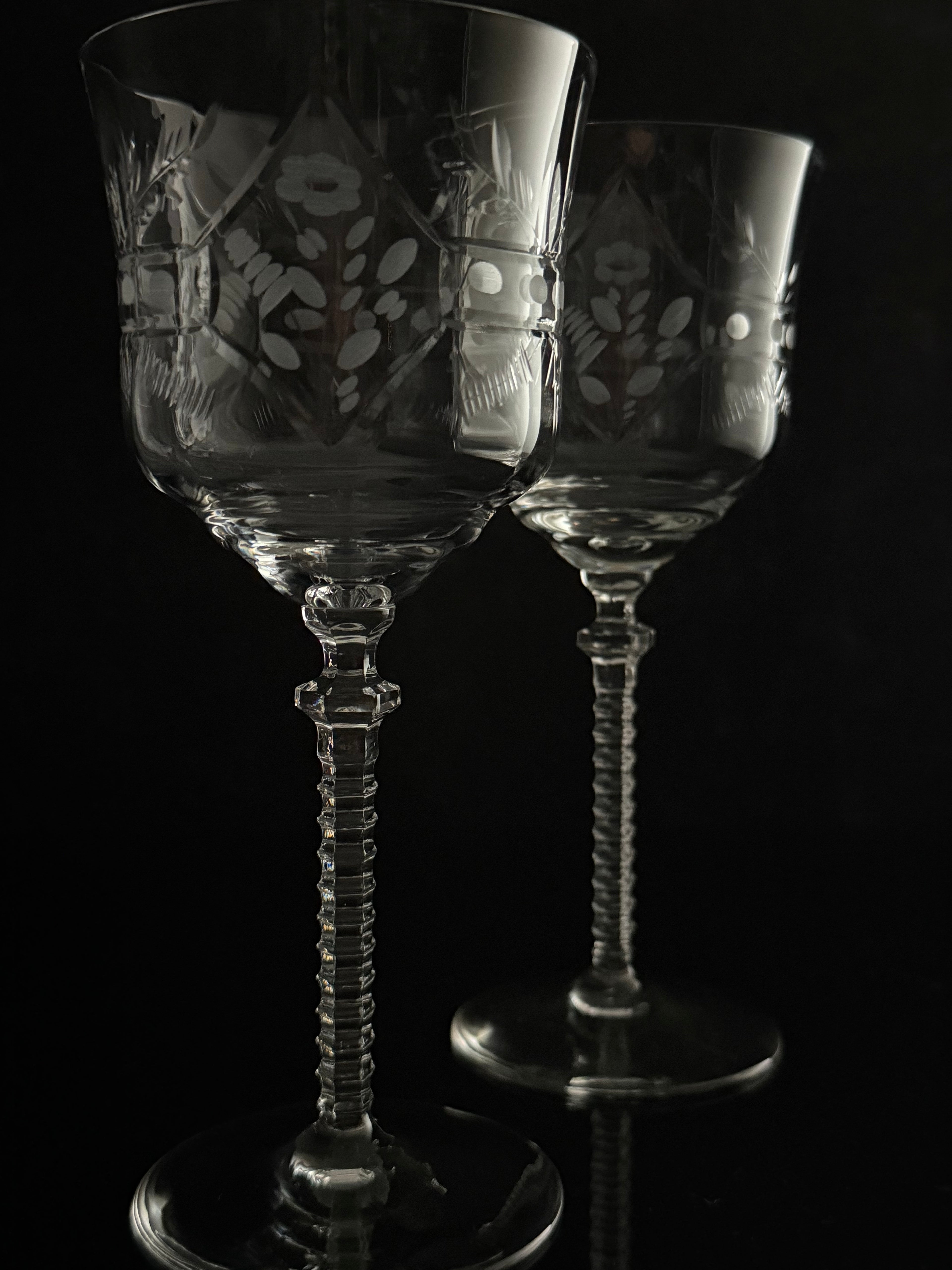 Two clear cut-glass wine glasses with floral engravings and twisted stems, photographed against a black background.