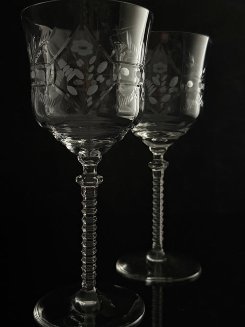 Two clear cut-glass wine glasses with floral engravings and twisted stems, photographed against a black background.
