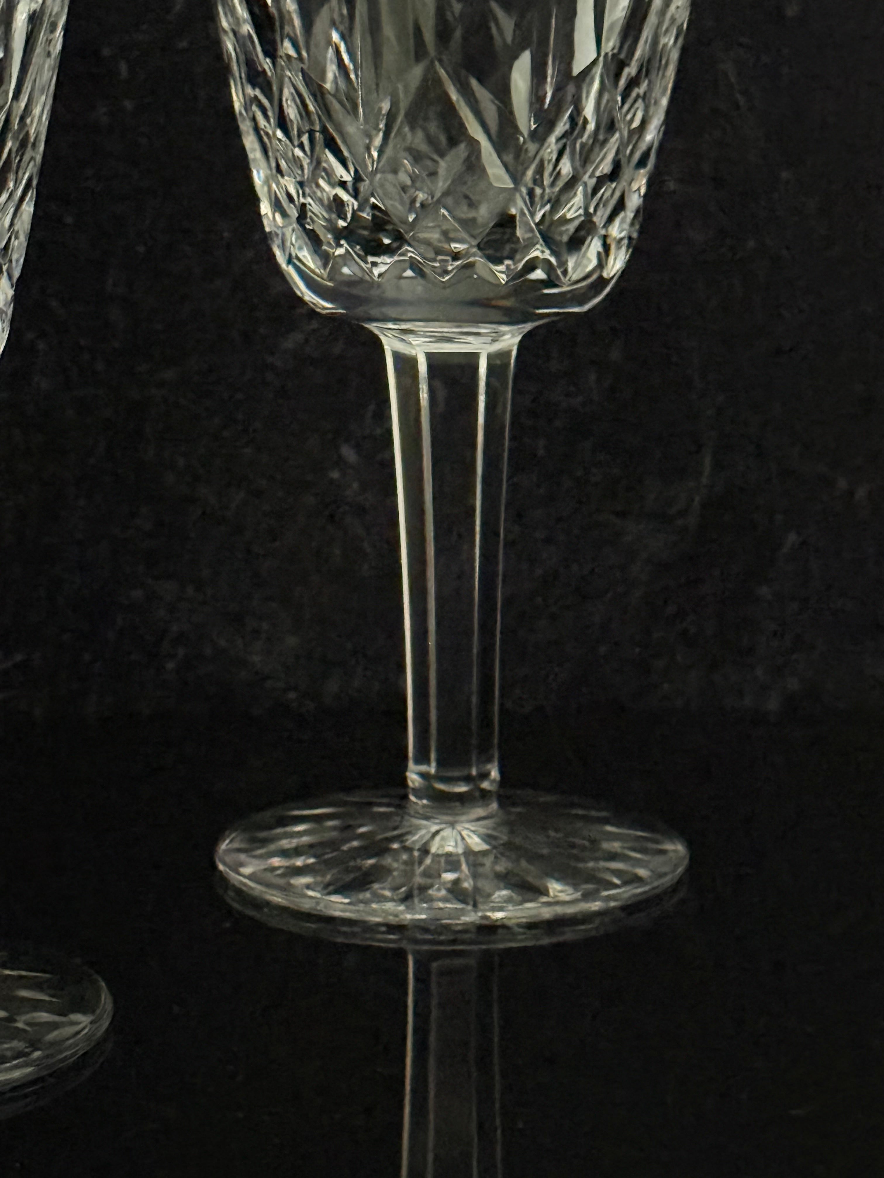 A close-up of a clear cut-crystal wine glass with a faceted stem and circular base, set against a dark reflective background.