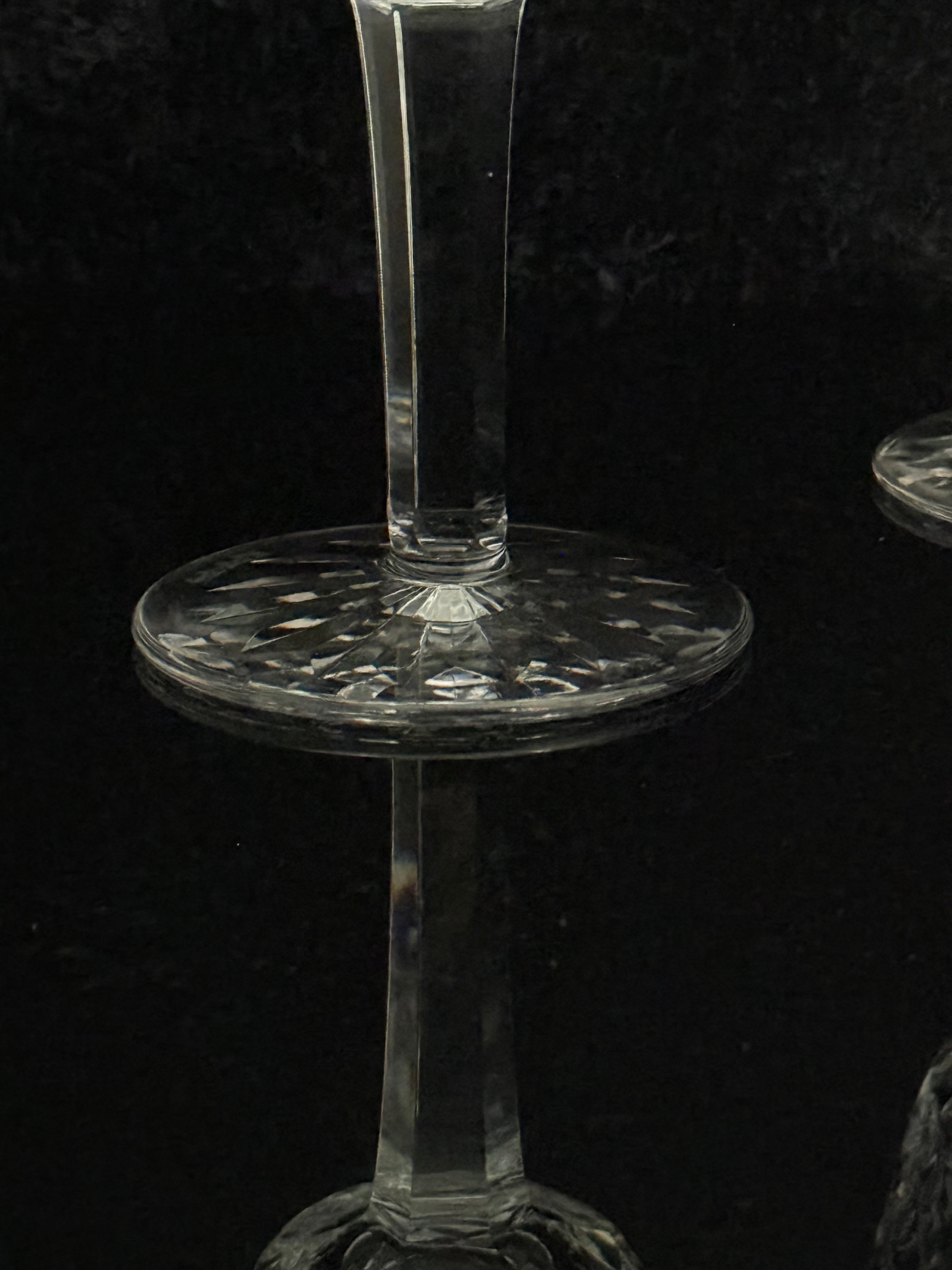 A close-up of a clear cut-glass candle holder or goblet with a circular patterned base and a narrow stem, shown against a dark black background.