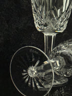 A close-up studio shot of a clear cut-crystal wine glass on a dark textured background, with part of another matching glass visible beside it.