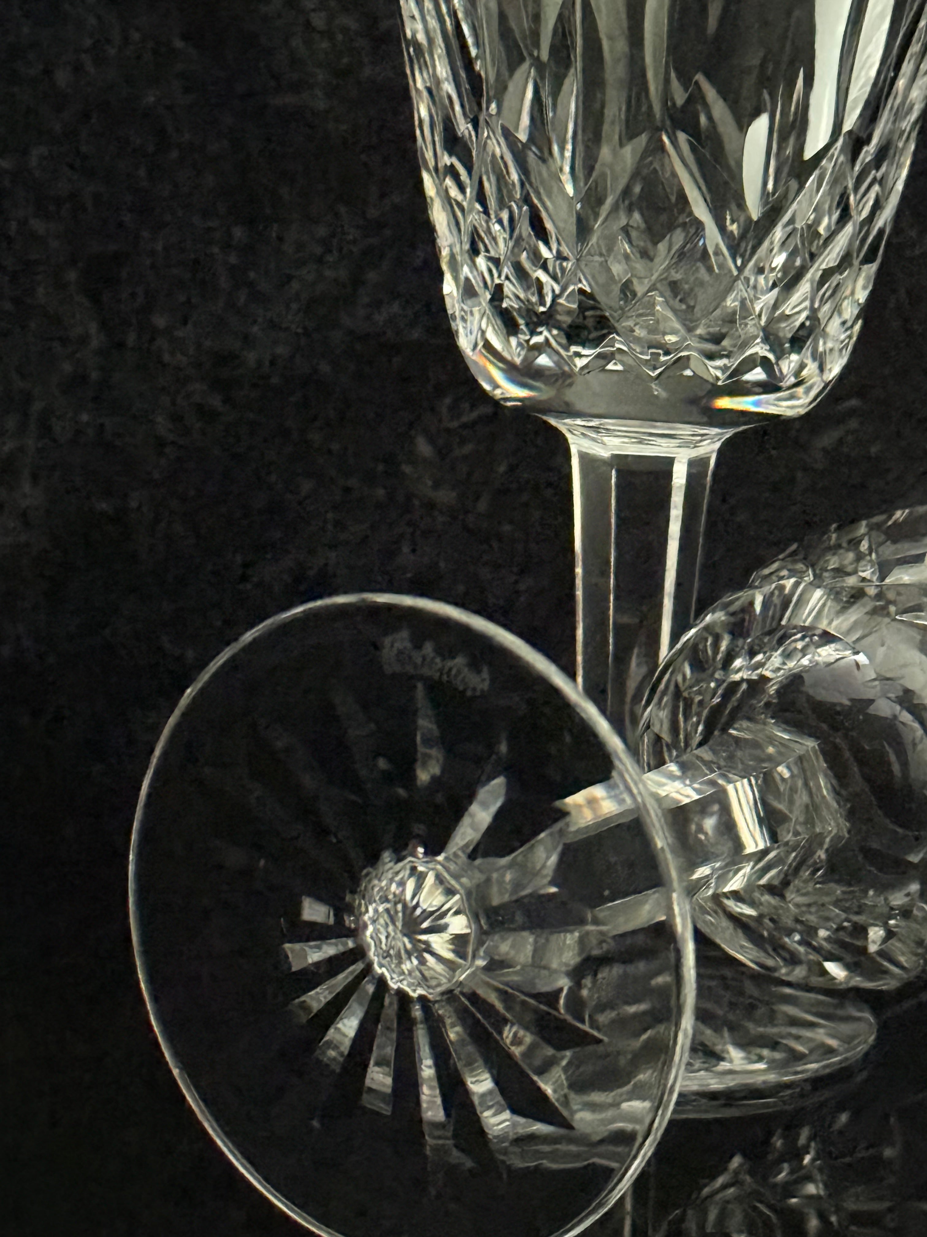 A close-up studio shot of a clear cut-crystal wine glass on a dark textured background, with part of another matching glass visible beside it.