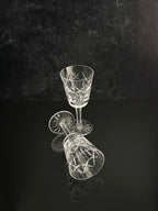 Two clear cut-crystal wine glasses on a reflective black surface against a dark textured background.