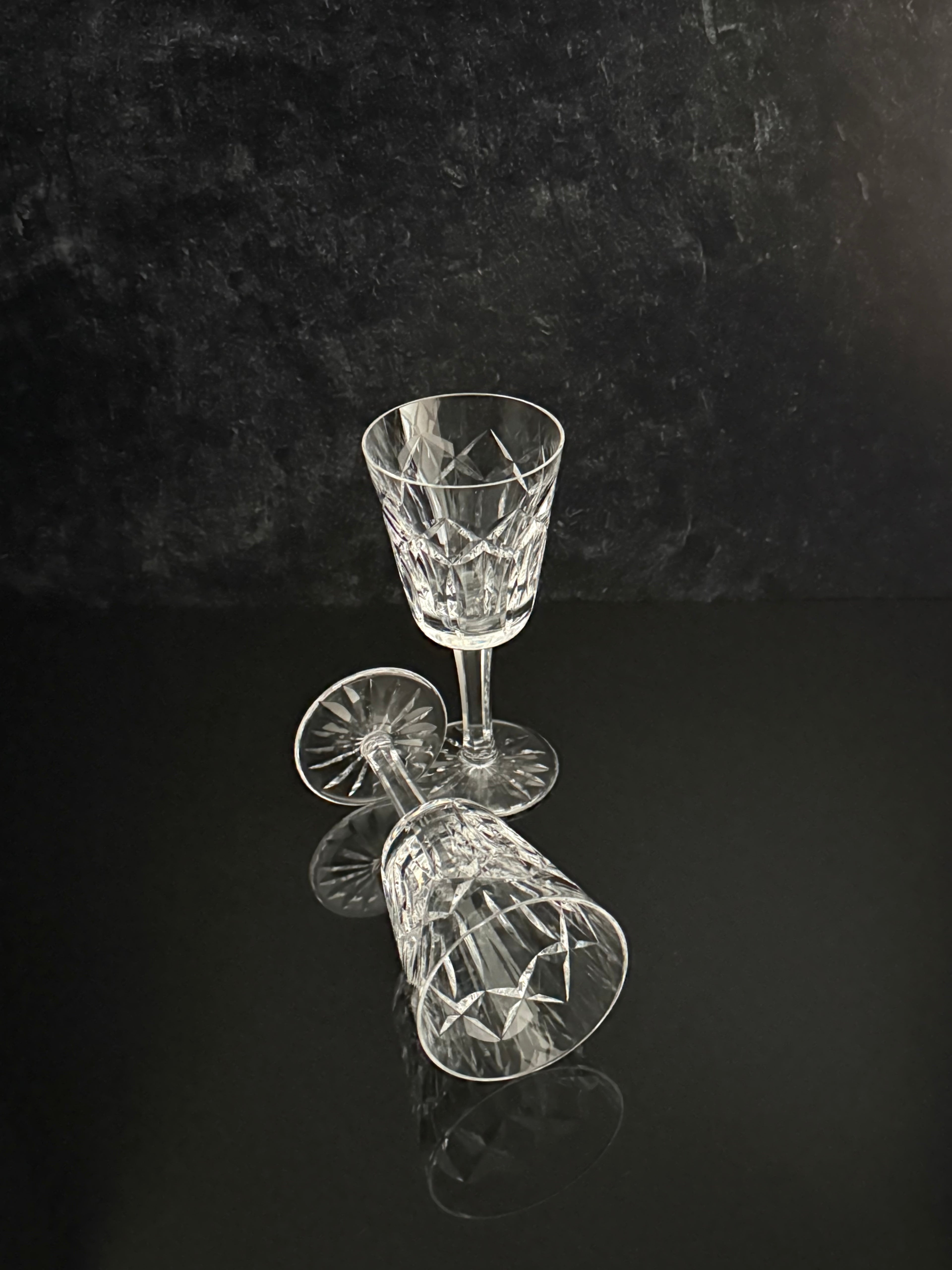 Two clear cut-crystal wine glasses on a reflective black surface against a dark textured background.