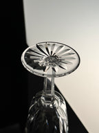 A close-up of a clear cut-crystal wine glass with a faceted starburst pattern on the bowl, photographed against a split black and white background.