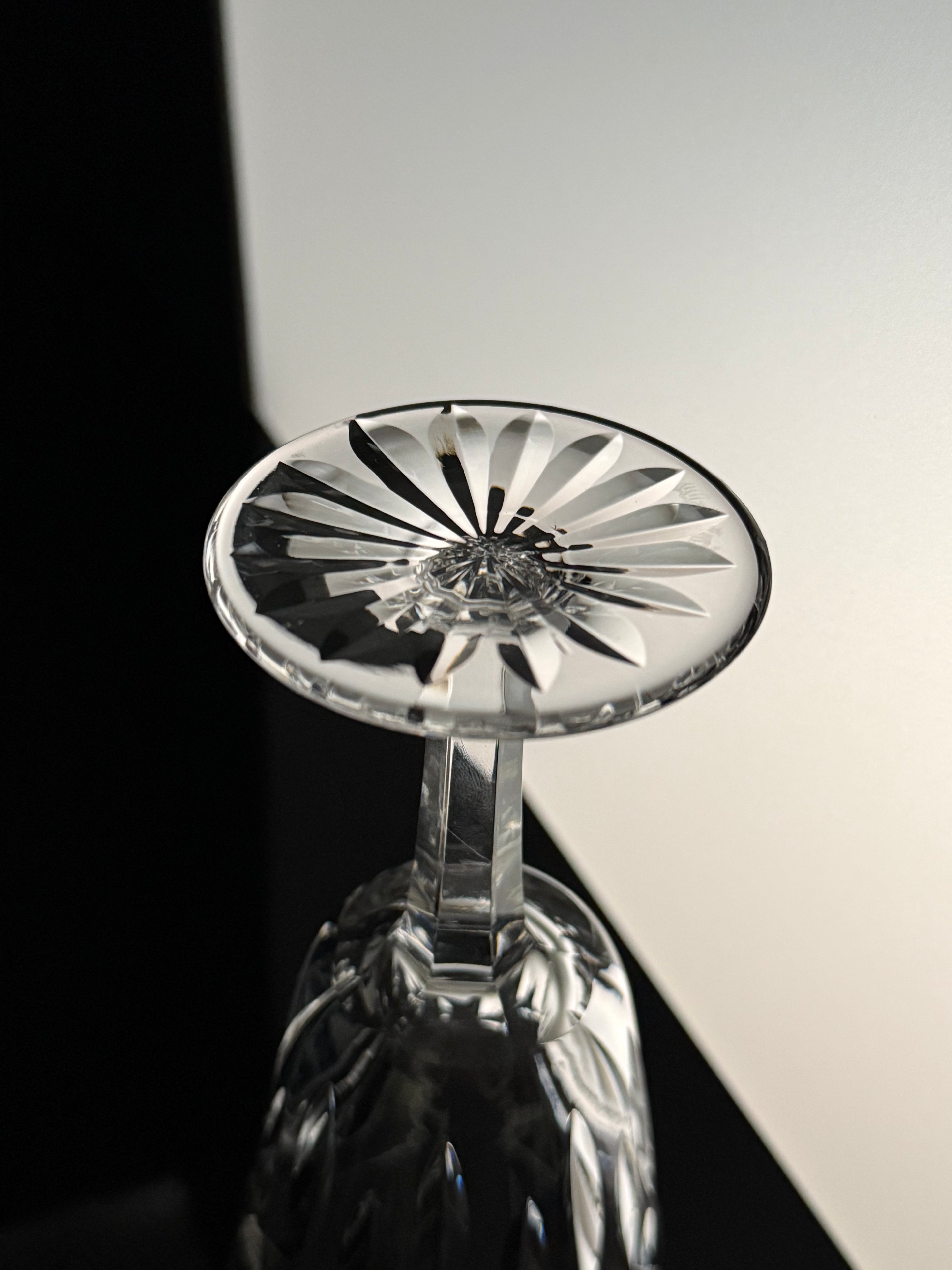 A close-up of a clear cut-crystal wine glass with a faceted starburst pattern on the bowl, photographed against a split black and white background.