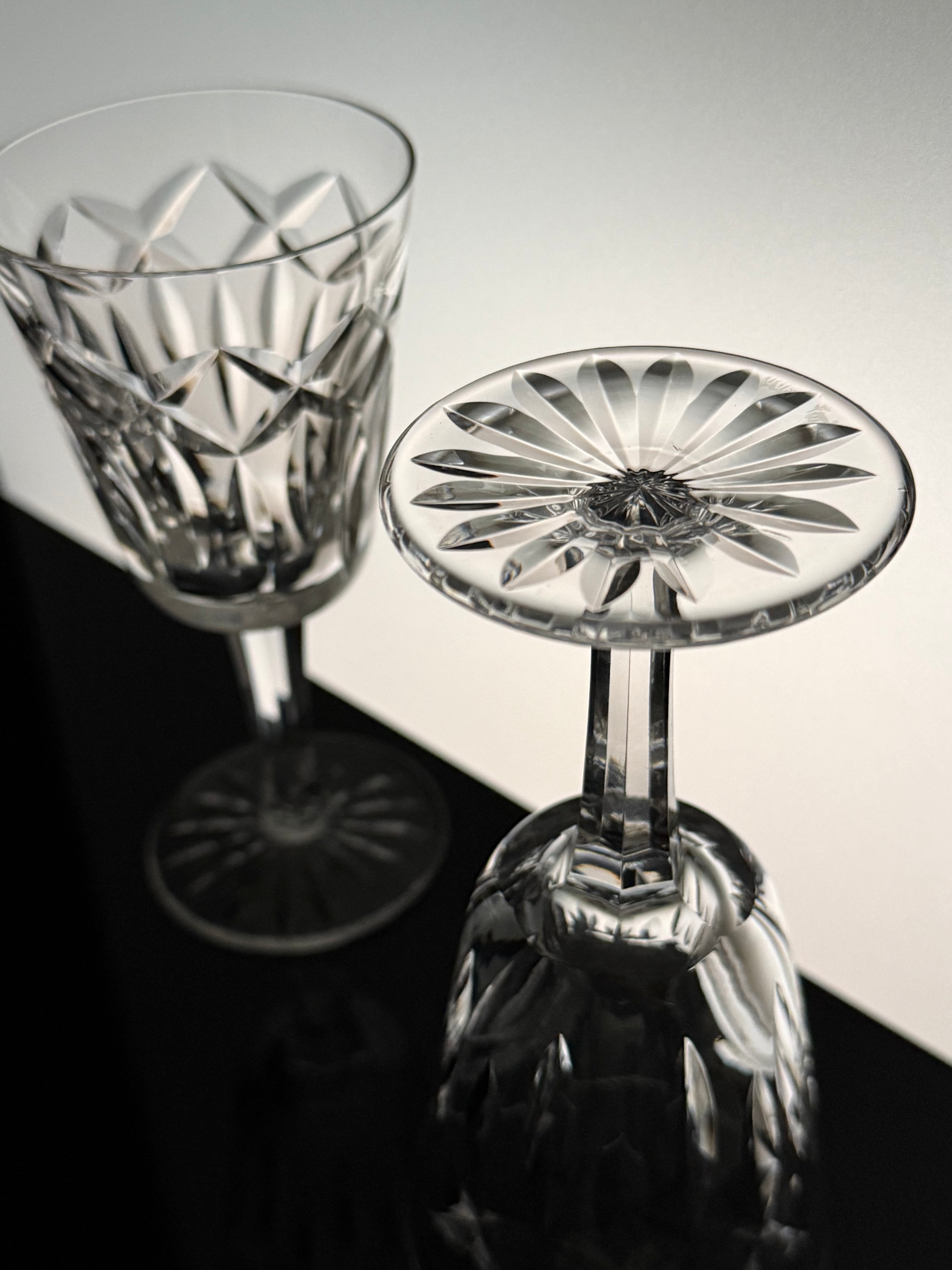 Two clear cut-crystal wine glasses with geometric and floral starburst patterns, one standing upright and the other tilted to show the bowl and stem, on a black and white background.