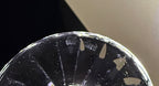 A close-up of a clear glass bowl or dish with a reflective rim, showing some smudges and reflections against a dark and light background.