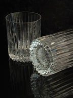 Two clear cut-crystal tumbler glasses on a glossy black reflective surface, one standing upright and the other lying on its side to show the faceted base pattern.