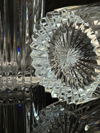 A close-up of a clear cut-glass or crystal object with a faceted starburst pattern, showing reflective highlights and dark reflections against a dark background.