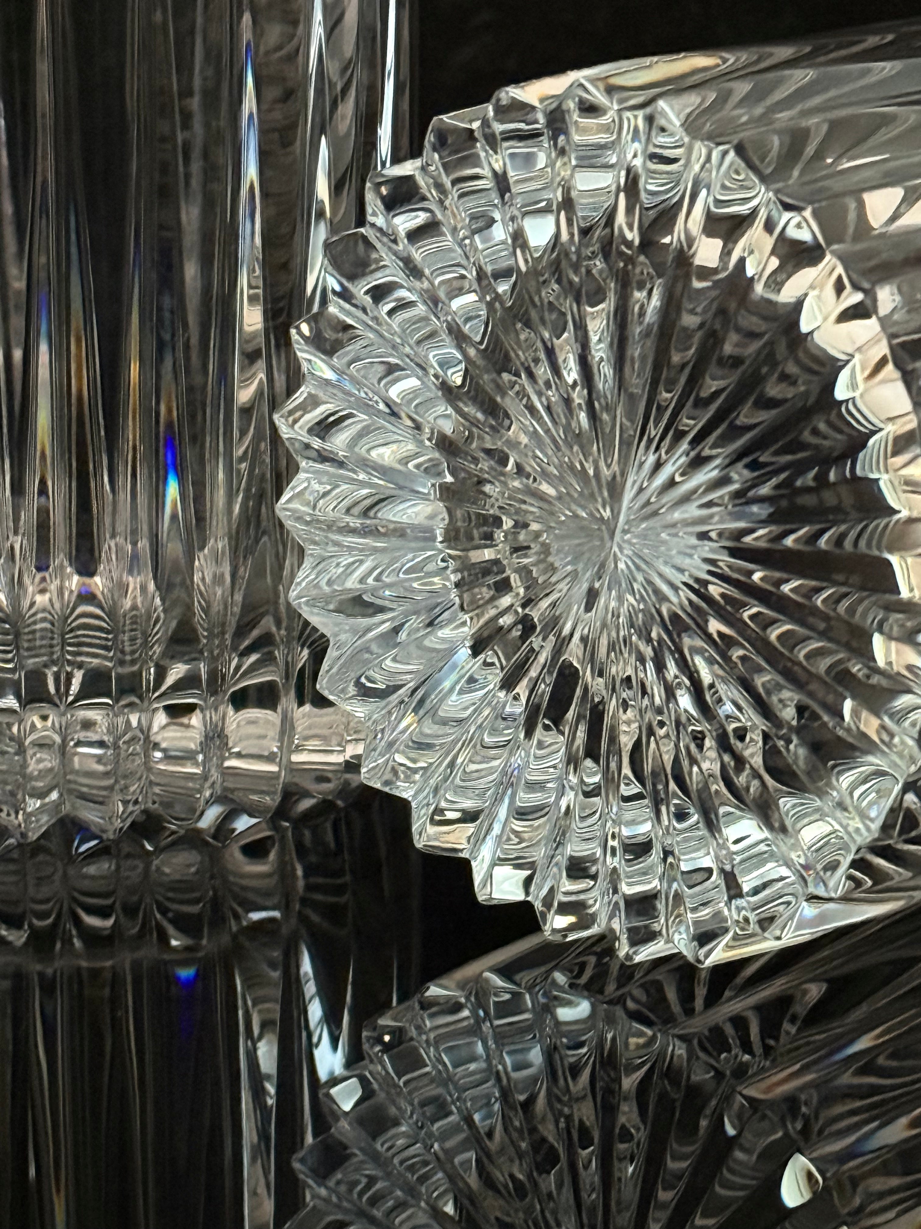 A close-up of a clear cut-glass or crystal object with a faceted starburst pattern, showing reflective highlights and dark reflections against a dark background.