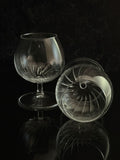 Two clear cut-crystal or glassware pieces on a black reflective surface against a dark background, one standing upright and one lying on its side to show the interior pattern.