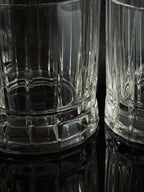 Clear ribbed glass tumblers with a faceted base, shown close up on a dark reflective surface.