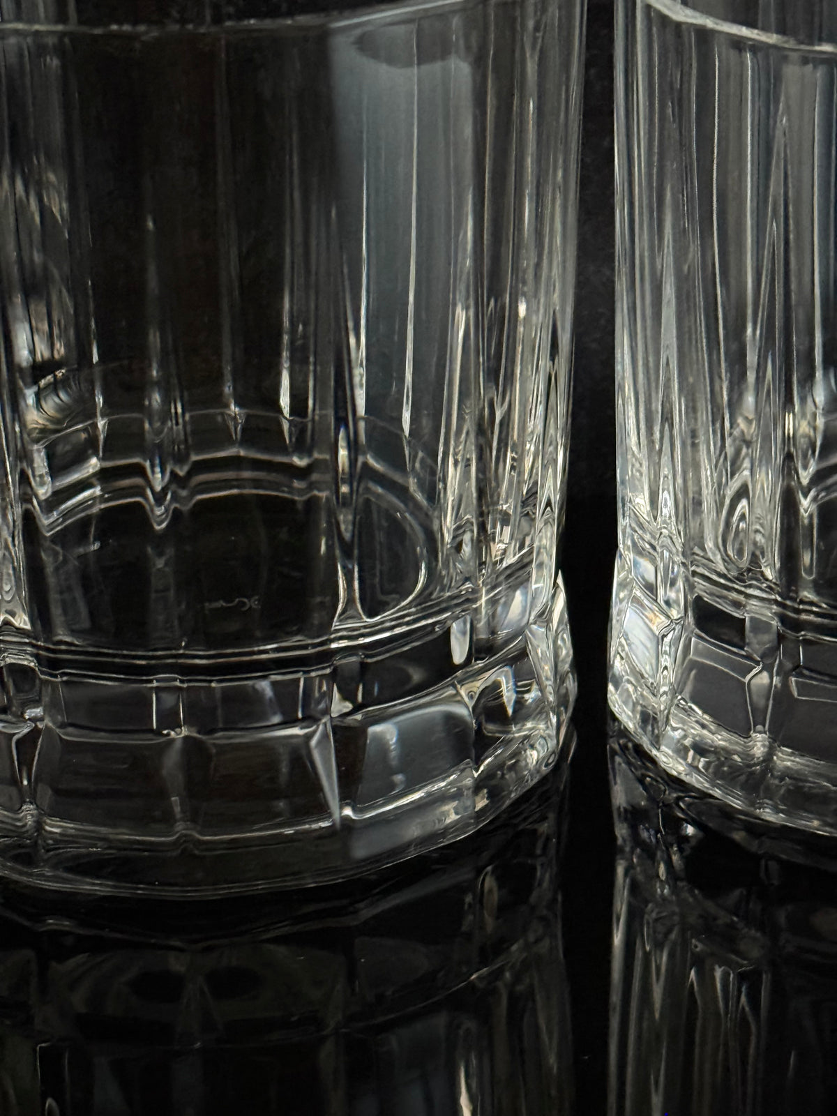 Clear ribbed glass tumblers with a faceted base, shown close up on a dark reflective surface.