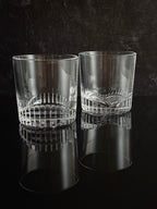 Two clear cut-crystal tumbler glasses with a textured patterned band around the middle, displayed on a dark textured background.