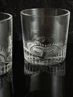 A close-up of a clear cut-glass tumbler with a textured patterned band, shown against a dark background.