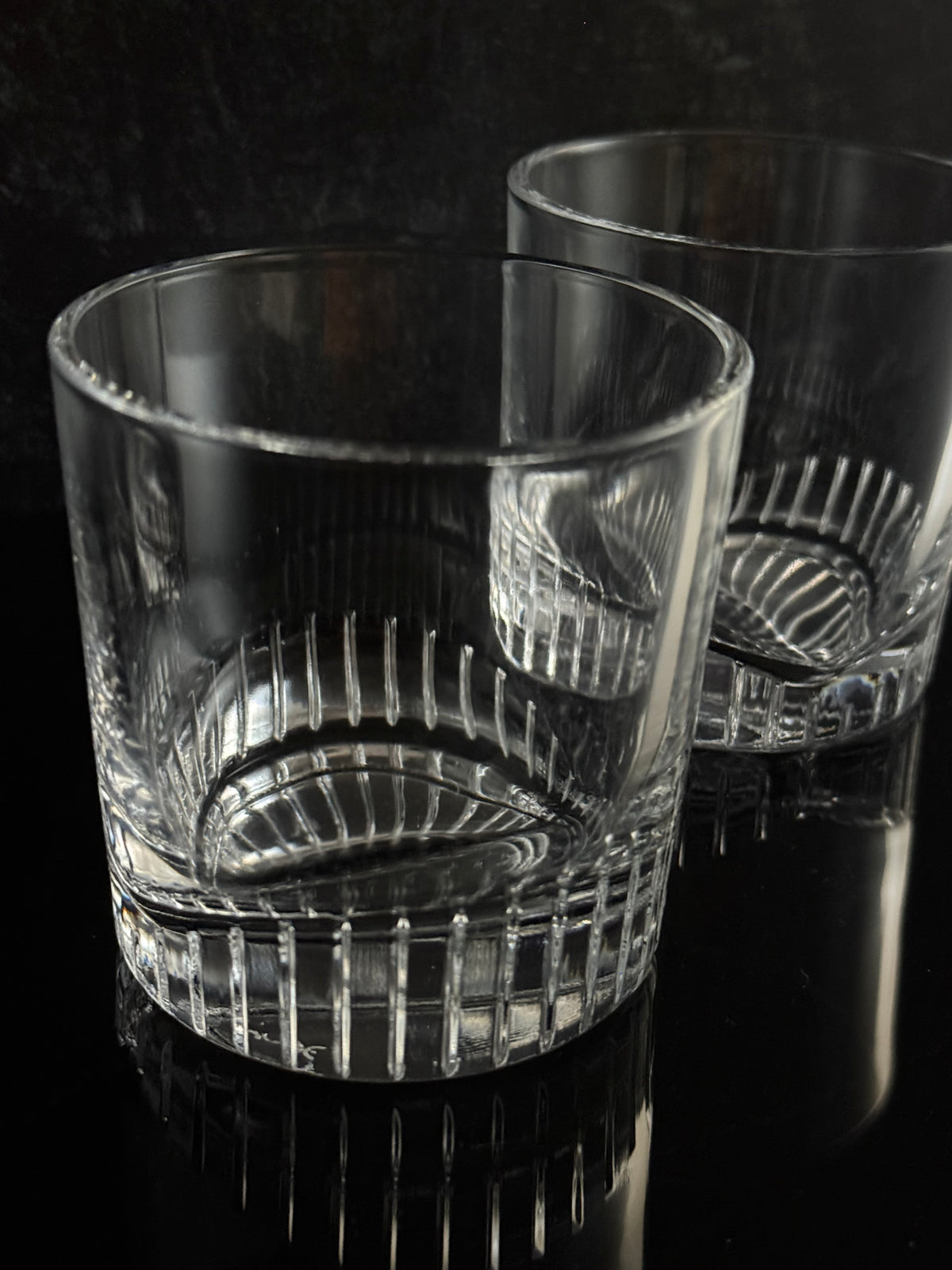 Two clear cut-crystal glasses with textured ribbed patterns, shown on a dark reflective surface.